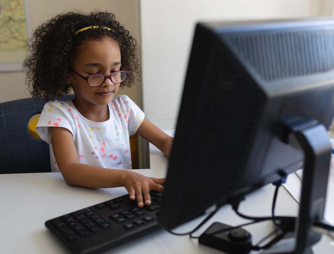 Front view little schoolgirl using desktop pc at desk in